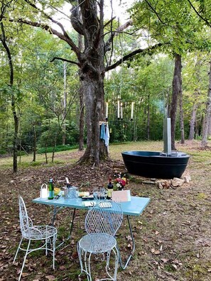 Une table de pique-nique avec des chaises, une bouteille, des verres et une petite table sur laquelle sont disposés de la nourriture et des boissons.