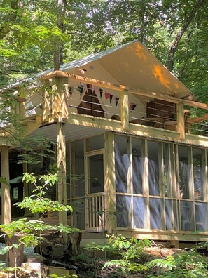 Une cabane en bois dotée d’une structure vitrée, entourée d’arbres.