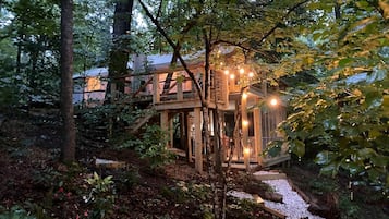 A wooden cabin with a glass door, surrounded by trees and a stone pathway.