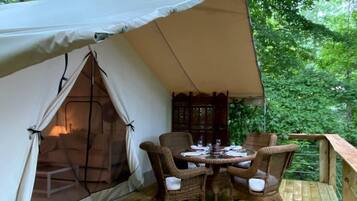 A tented accommodation with a wooden deck, wicker furniture, and a view of the surrounding forest.