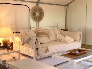 Un lit blanc à baldaquin, une table de chevet avec une lampe et un panier en osier posé sur une table en verre.