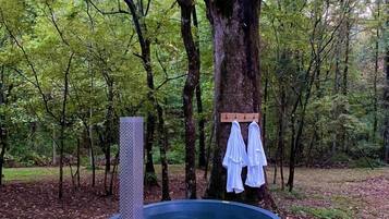 A hot tub in a forest setting with a wooden platform and towels hanging on a tree.