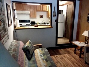 A compact living space with a kitchenette, a sofa, a small table, and a door leading to a bathroom.
