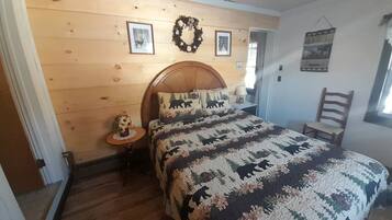 Une chambre à coucher avec une tête de lit en bois, un lit recouvert d’une couvre-lit à motifs, une petite table ronde ornée d’un vase et une chaise.
