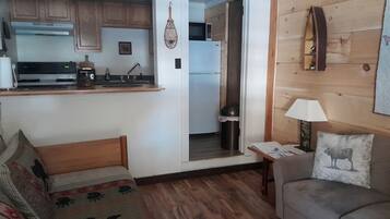 A compact living space with a kitchenette, a sofa, a small table, and a lamp.