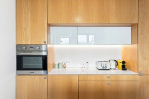 A kitchen with wooden cabinets, a built-in oven, a microwave, a toaster, a kettle, and a yellow appliance on the counter. - Ceuta Apartment | Charming Balcony Overlooking Porto's Rooftops   (Porto)