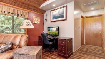 A room with a leather sofa, a wooden desk with a computer, a lamp, and a framed picture on the wall.