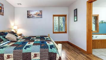 A bedroom with a bed, a window, a painting, and a bathroom visible through an open door.