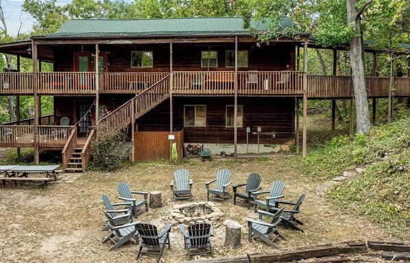 A cabin with a two-story deck, outdoor seating, and a fire pit.