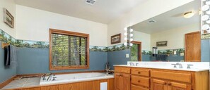 Une salle de bain dotée d’une grande fenêtre, d’un meuble-lavabo en bois et d’un miroir avec éclairage intégré.