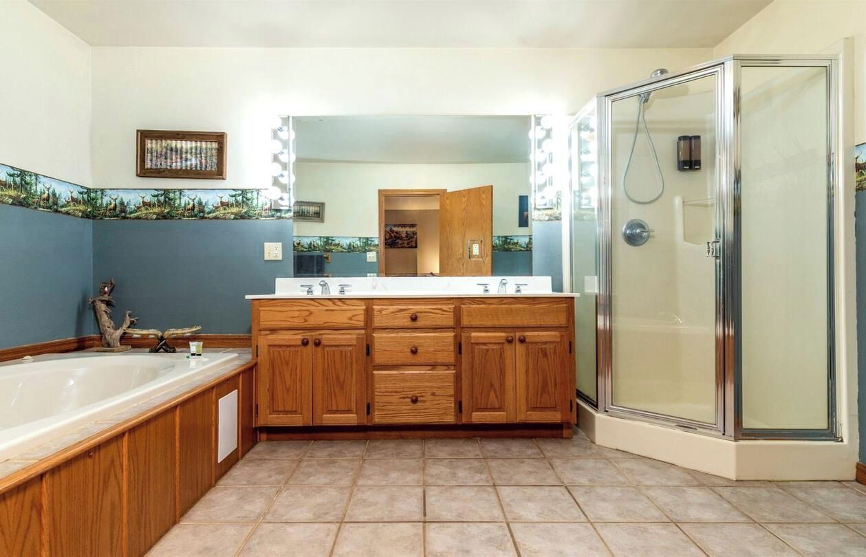 A bathroom with a large wooden vanity, a bathtub, a glass shower enclosure, and a mirror with lights.