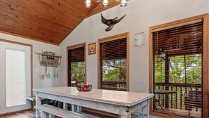 A room with a wooden ceiling, a table with a fruit bowl, and windows with blinds.