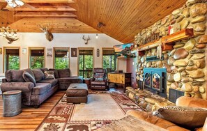 L’intérieur chaleureux d’un chalet avec une cheminée en pierre, des fauteuils confortables et un plafond orné de poutres en bois.