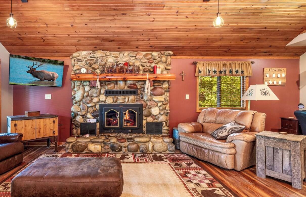 A cozy living room with a stone fireplace, leather sofa, and a television mounted on the wall.