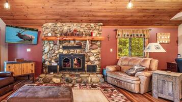 A cozy living room with a stone fireplace, leather sofa, and a television mounted on the wall.