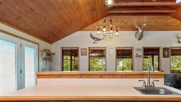 A kitchen with a large island, wooden ceiling, and deer antlers on the wall.