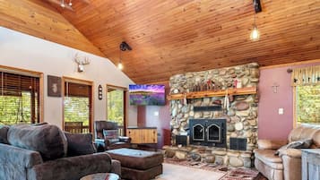A cabin interior with a stone fireplace, wooden ceiling, and rustic decor.