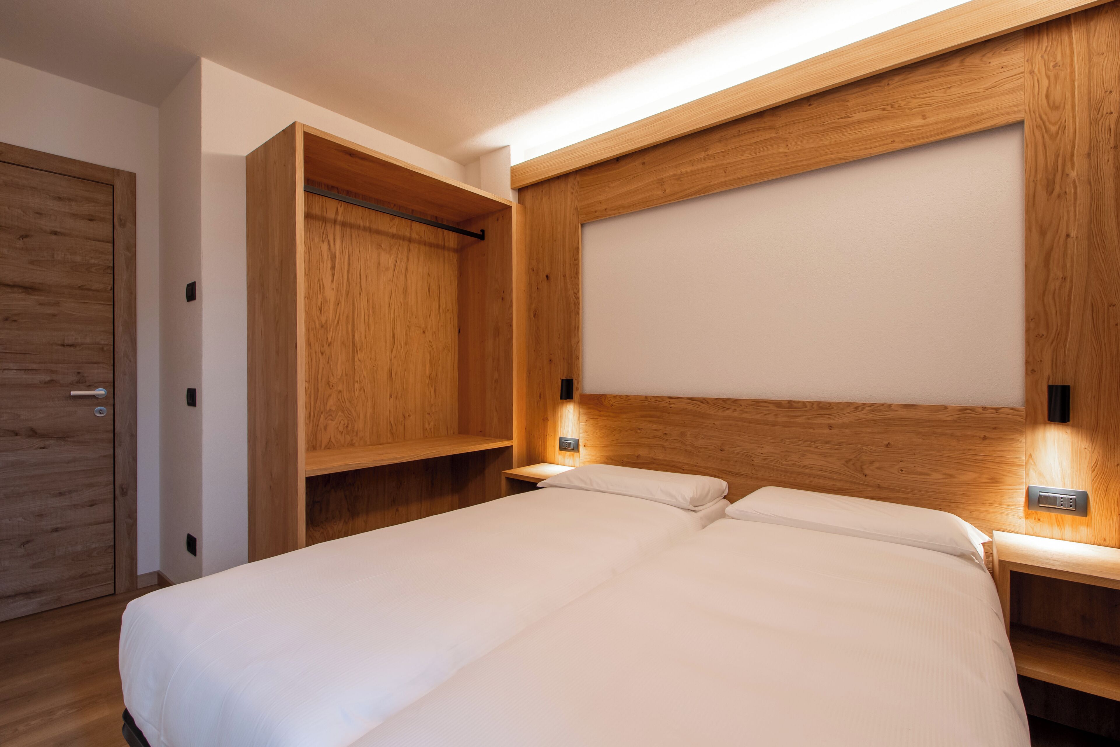 Une chambre à coucher moderne avec un grand lit, une tête de lit en bois, des tables de chevet avec des lampes et une armoire.