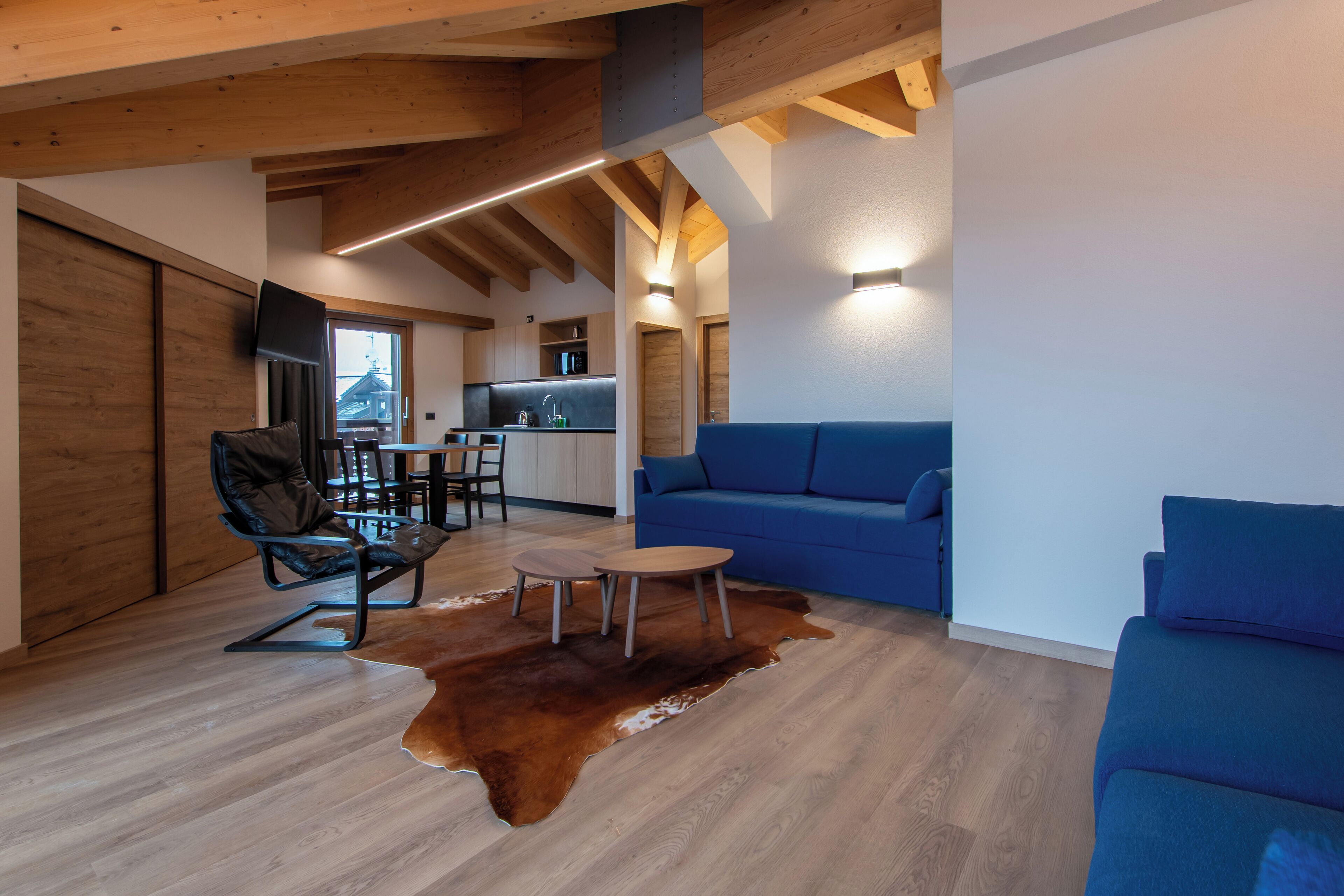 A modern interior with a wooden ceiling, a blue sofa, a dining area, and a kitchen.
