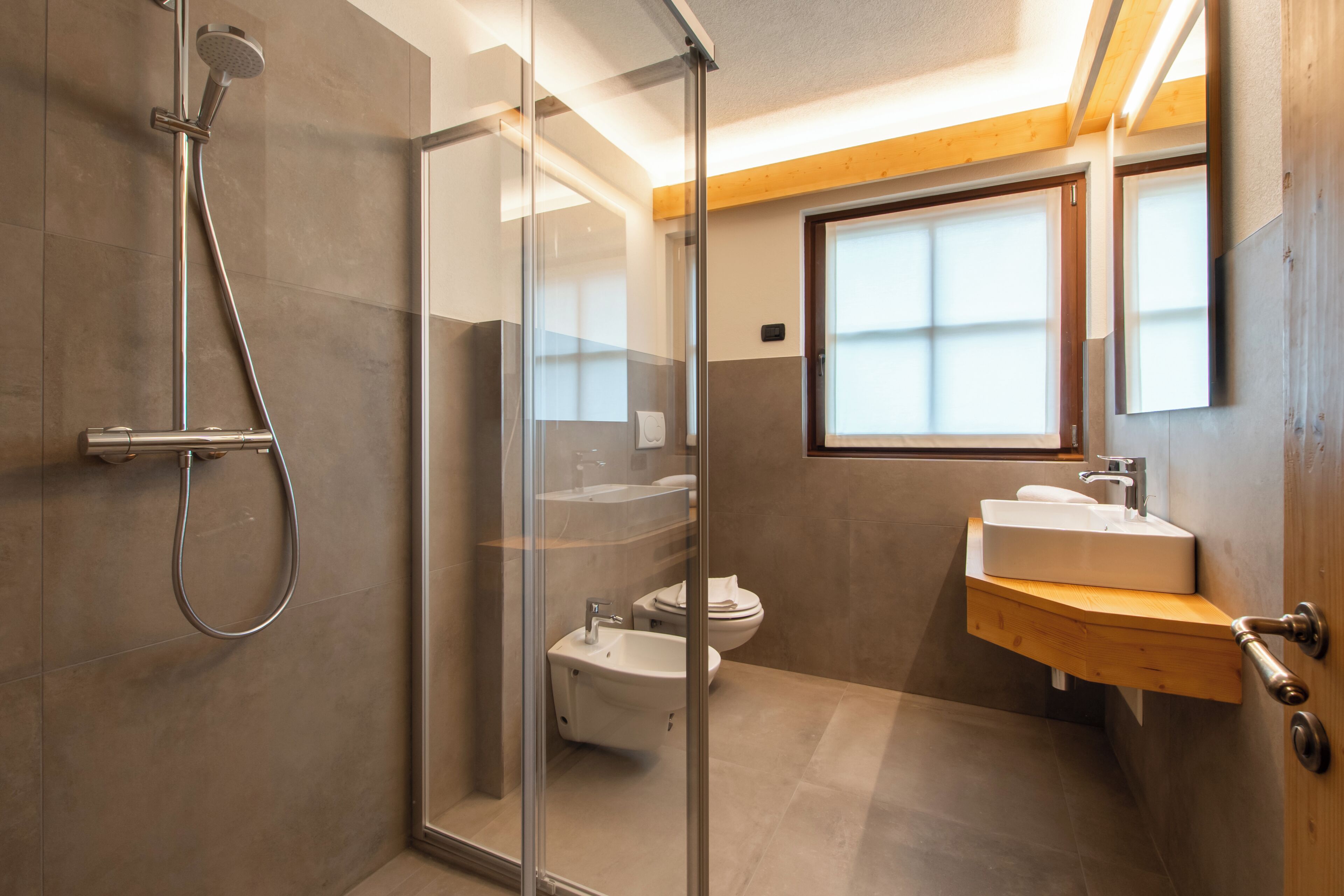 A modern bathroom with a glass shower enclosure, a toilet, and a sink with a wooden countertop.