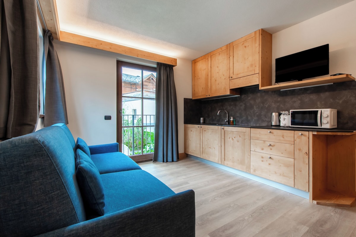 A modern kitchen with wooden cabinets, a built-in microwave, and a television on a shelf.