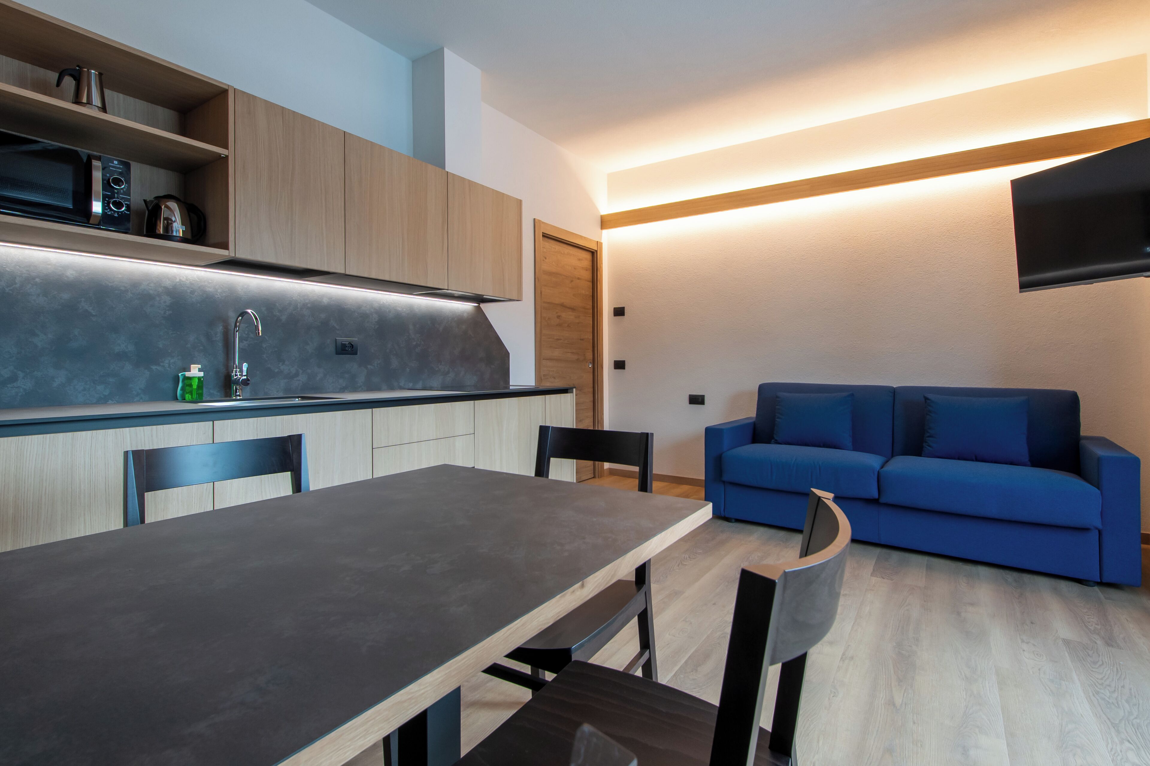A modern kitchen with wooden cabinets, a dining table, and a blue sofa in a compact living area.
