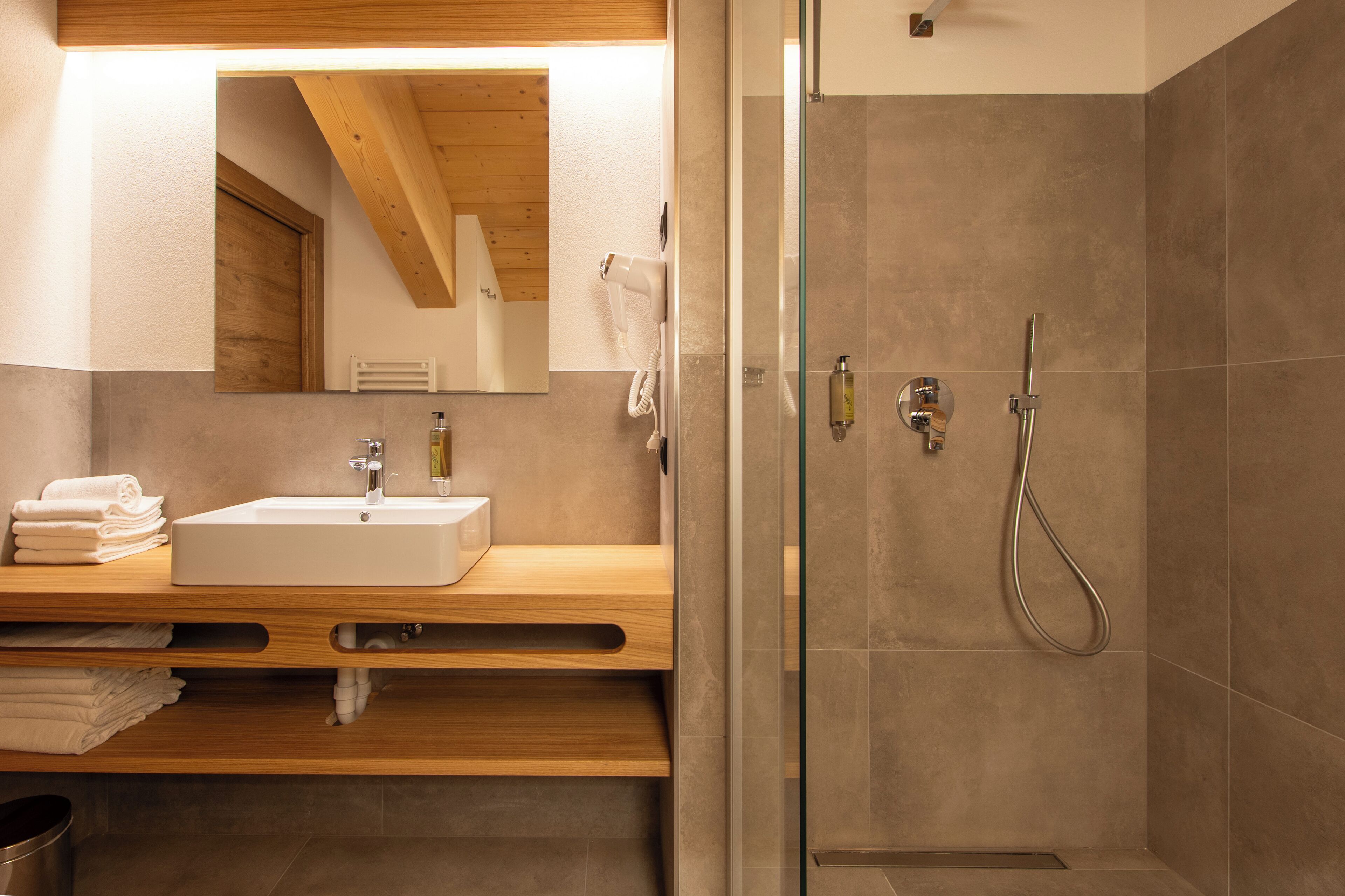 A modern bathroom with a wooden vanity, a large mirror, a sink, and a glass-enclosed shower area.