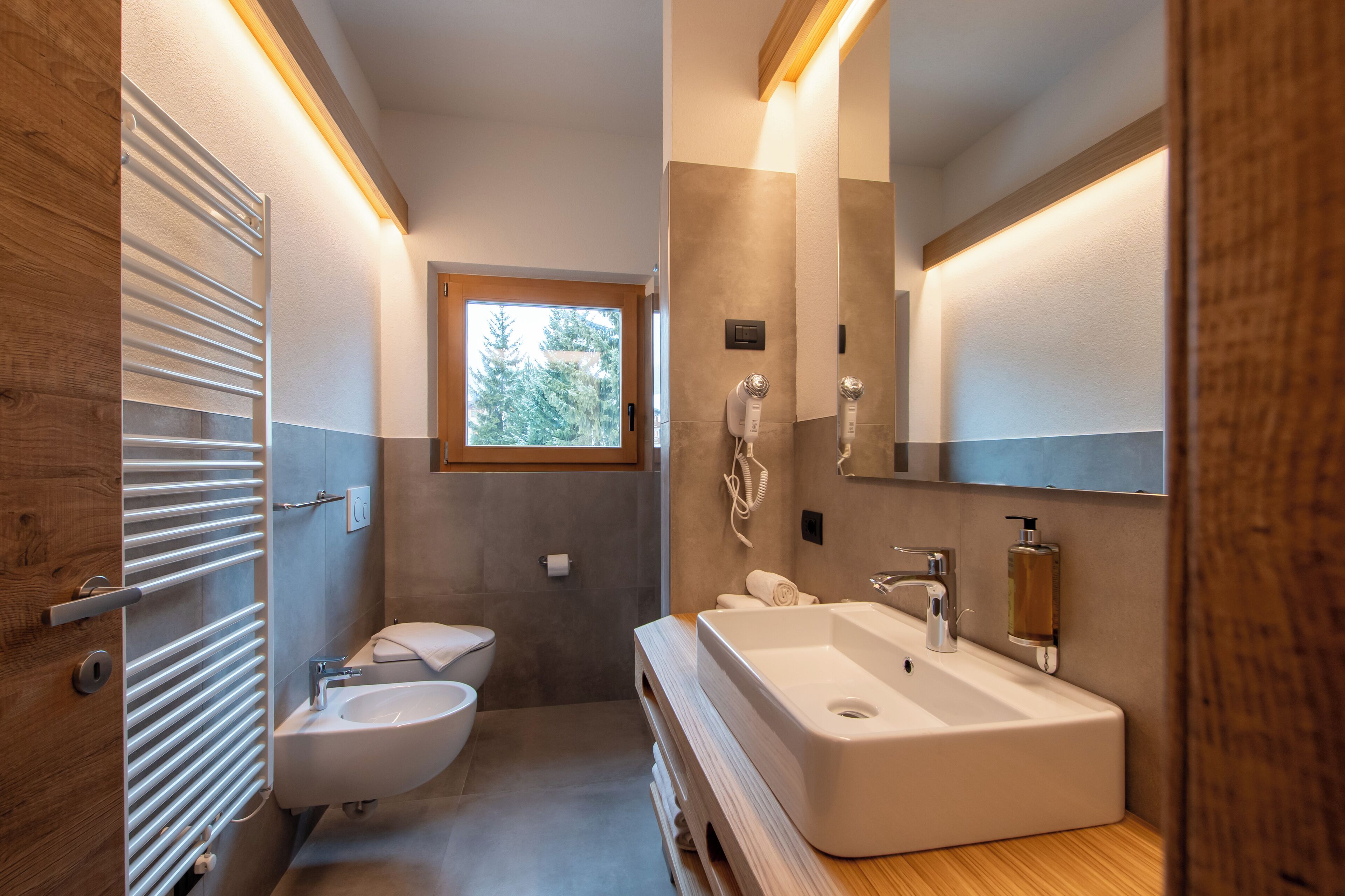Een moderne badkamer met een houten wastafelmeubel, een grote spiegel, een inbouwwastafel en een toilet.