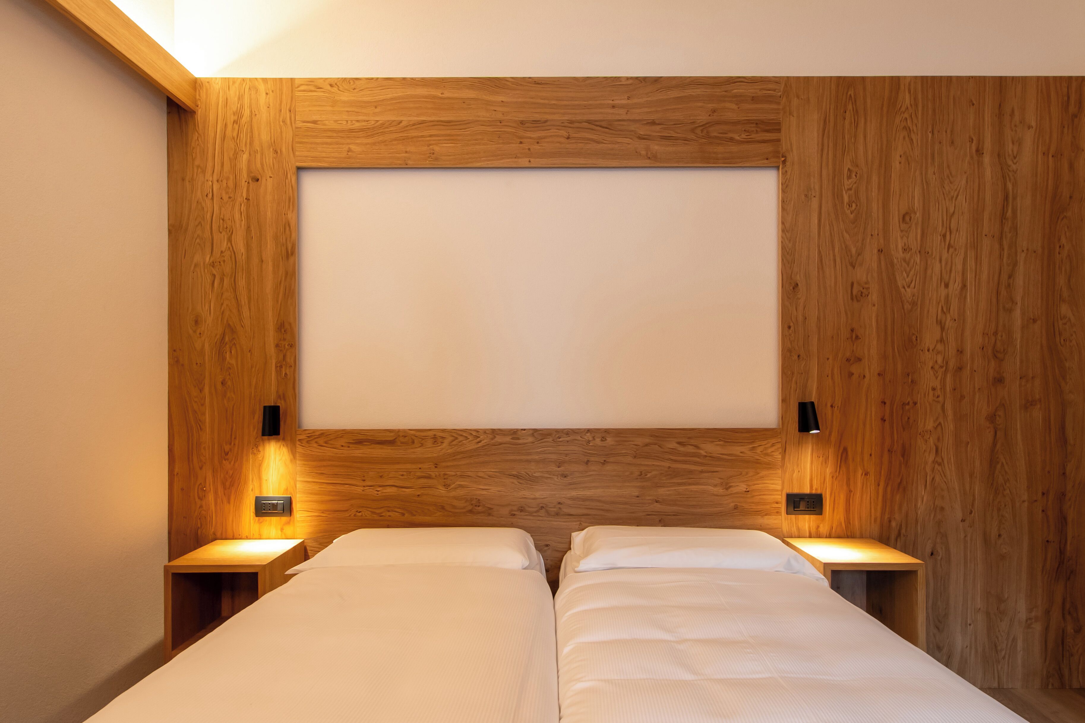 A double bed with wooden headboard and nightstands, each with a wall-mounted light.