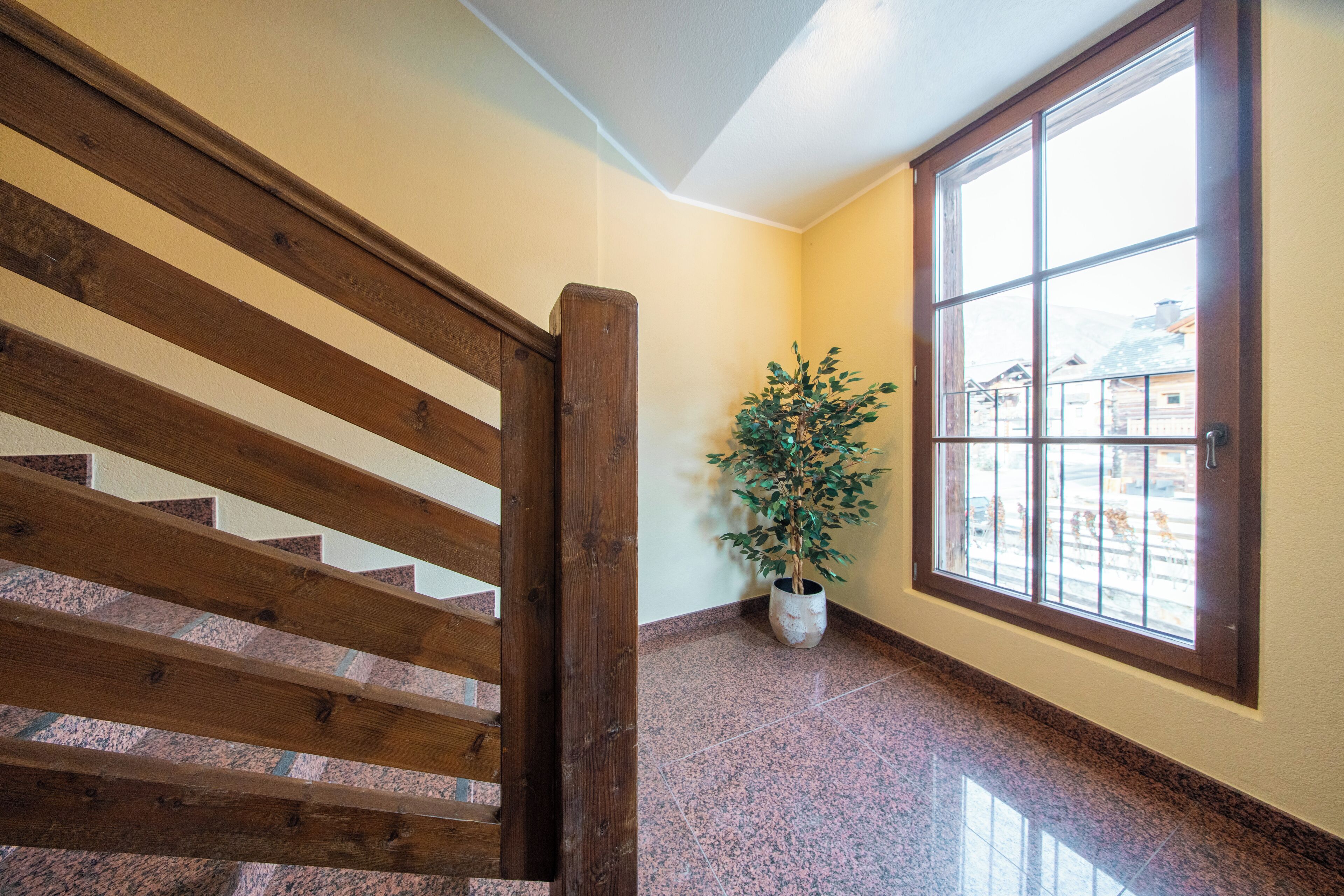 Eine Holztreppe führt zu einer Zwischenebene mit einem Blumentopf und einem großen Fenster.