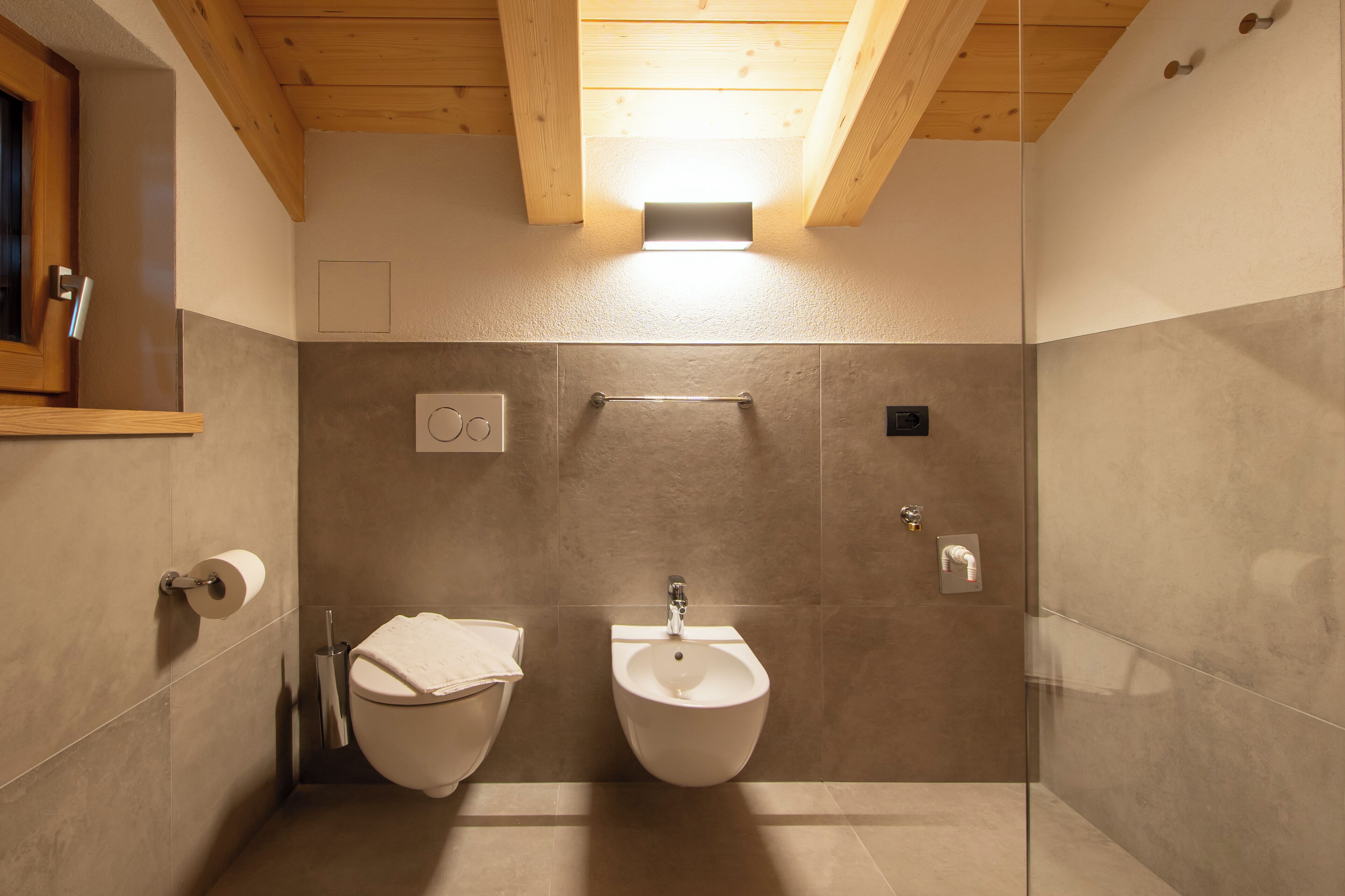 A modern bathroom with two toilets, a bidet, and a towel rack.
