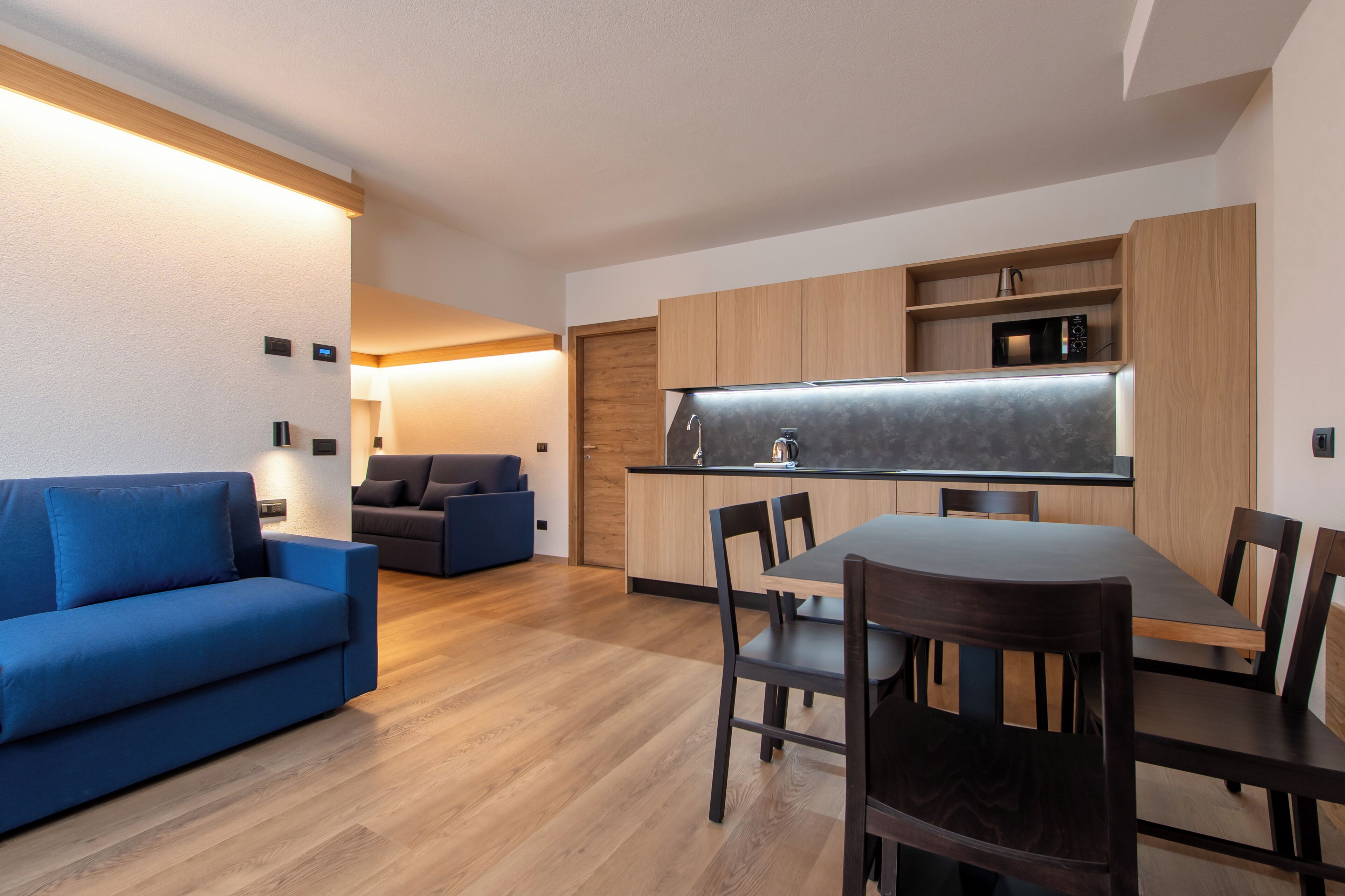 A modern kitchen with wooden cabinets, a built-in microwave, and a dining area with a table and chairs.