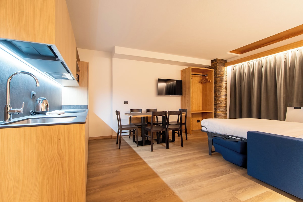 A compact hotel room with a kitchenette, a dining area, and a bed.
