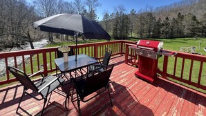 Um deck com mesa, cadeiras, churrasqueira e vista para uma área arborizada.