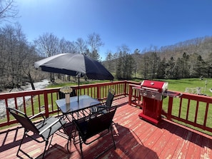 Eine Terrasse mit Tisch, Stühlen, einem Grill und Blick auf ein bewaldetes Gebiet.