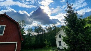 Um celeiro vermelho e uma casa branca, com um gramado e árvores ao fundo.