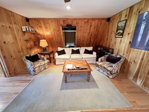 Een kamer met houten lambrisering, een zithoek, een salontafel en een vloerkleed.