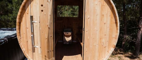 A wooden barrel-shaped structure with a door, a small window, and a visible interior with a bench and a fireplace.