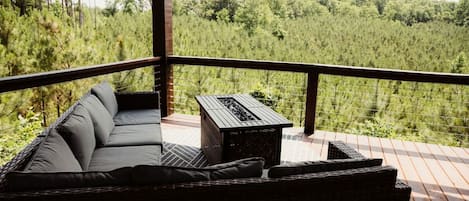 A balcony with a wicker sofa and a small table, overlooking a forested area.