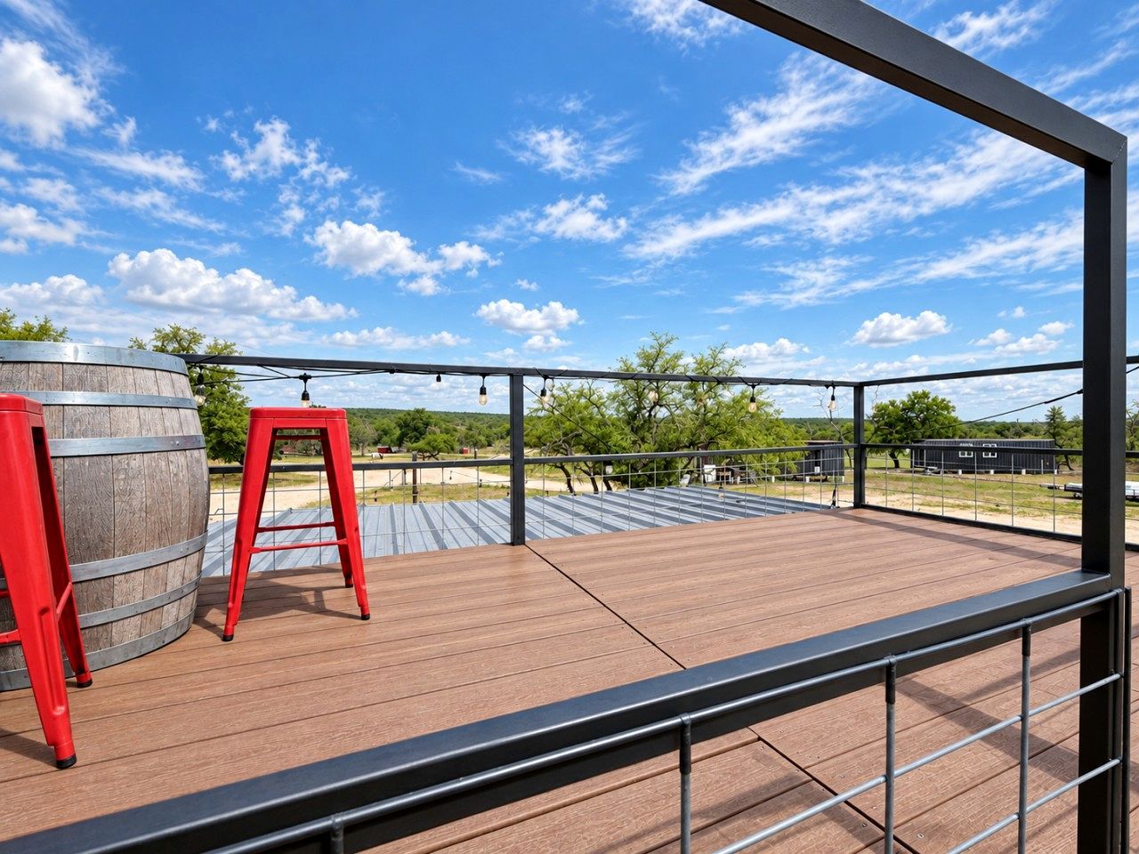 Une terrasse extérieure avec un plancher en bois, une rambarde en métal et un tabouret rouge.