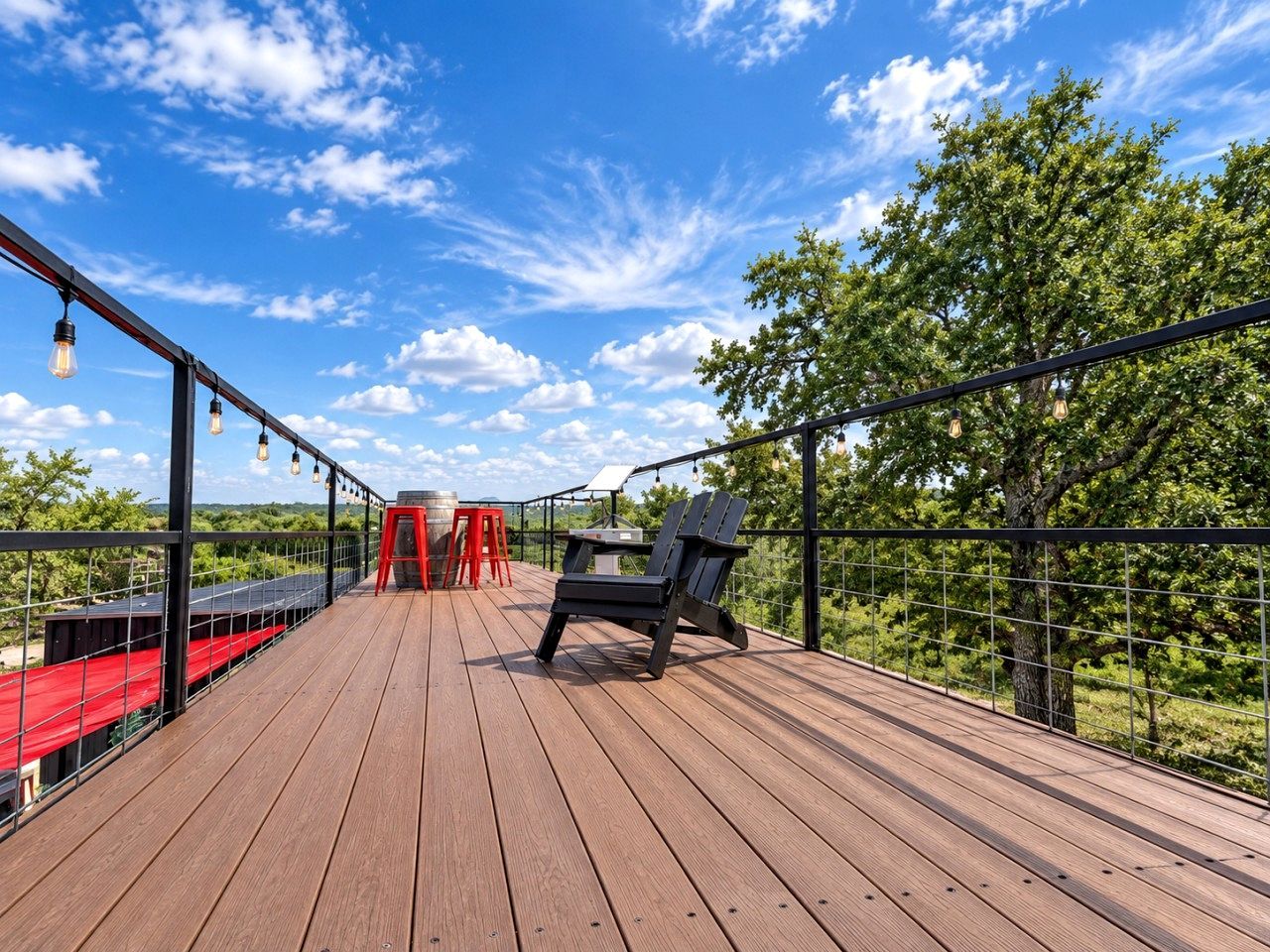 A wooden deck with a red table and chairs, a black chair, and hanging light bulbs.