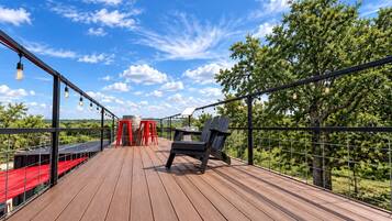 A wooden deck with a red table and chairs, a black chair, and hanging light bulbs.