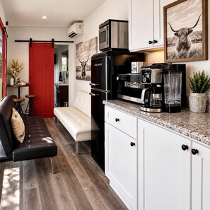 A compact kitchen with a refrigerator, microwave, coffee maker, and a dining area with a bench and stools. - Wonderful Secluded Container in Fredericksburg, Texas (Fredericksburg)