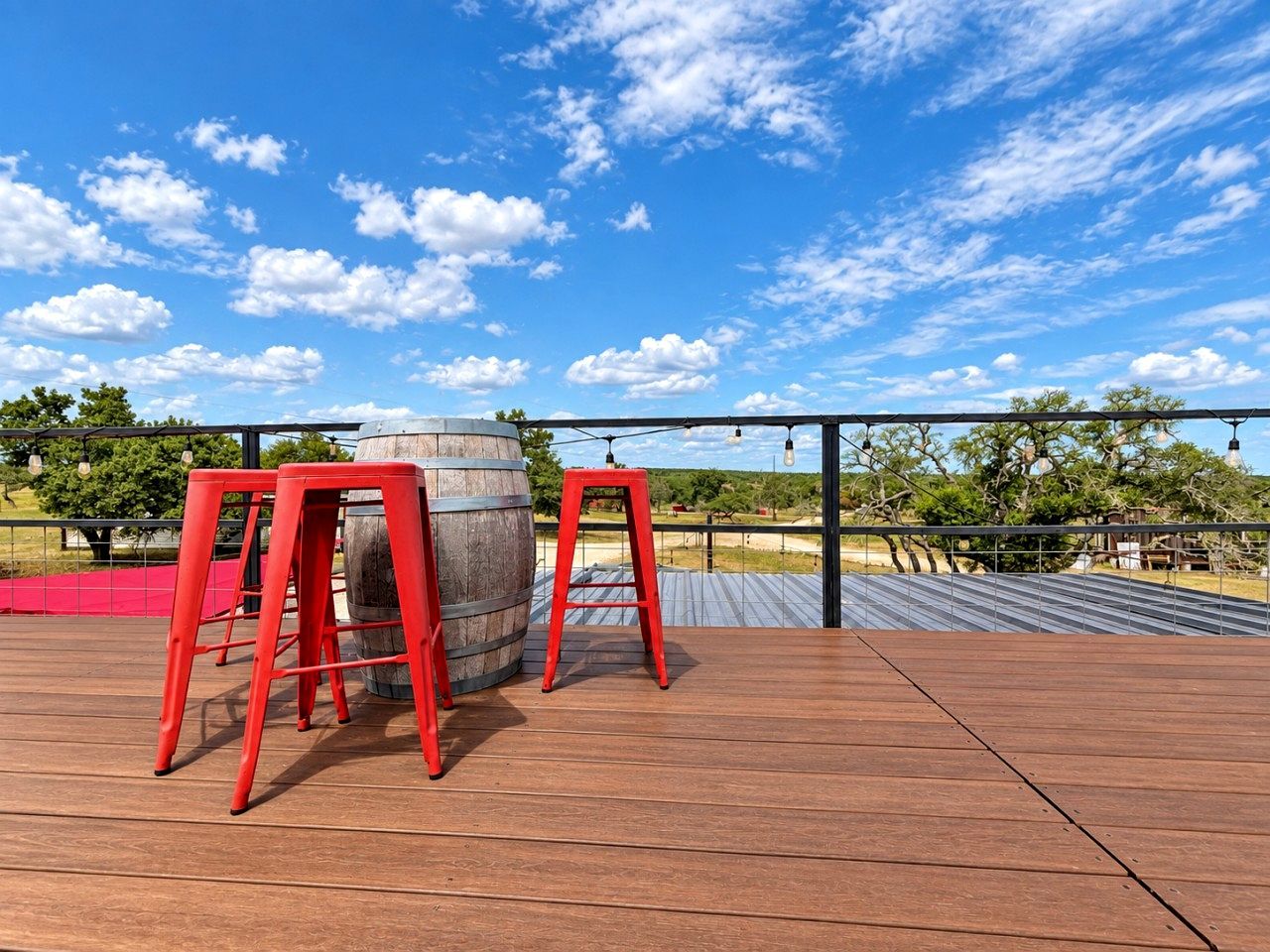 An outdoor deck with wooden flooring, two red stools, and a barrel.