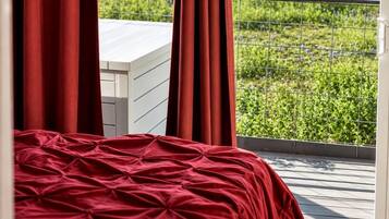 A bedroom with a bed, red curtains, and a view of a green field through a balcony railing.