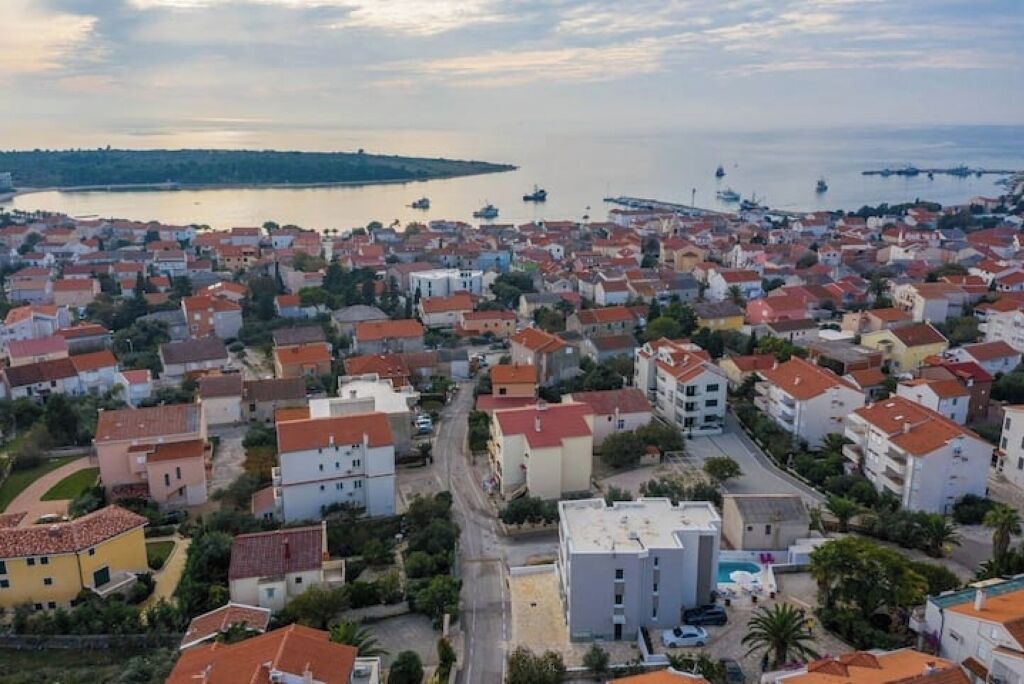 Vista aérea de un pueblo costero con viviendas densas, un puerto deportivo con barcos y una vista despejada del mar.