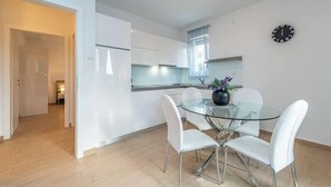 A modern kitchen with white cabinets, a glass dining table, and white chairs. - Star house 1 (Novalja)