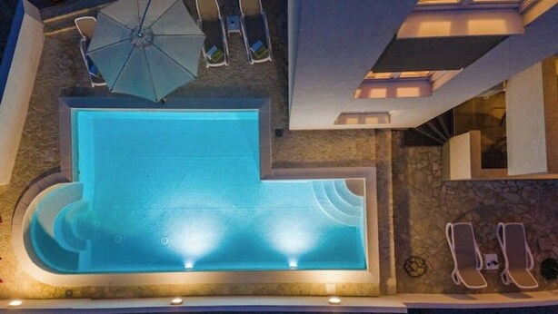 An indoor swimming pool with a stone wall, lounge chairs, and an umbrella. - Star house 1 (Novalja)