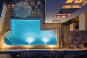 Una piscina interior amb pared de pedra, seients de relaxació i una ombrell.