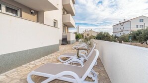 A row of white sun loungers on a stone patio with a white building in the background. - Star house 1 (Novalja)